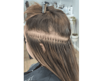 Woman with brown hair getting hair extensions applied in a salon by Hair by Jessie Lu, with small sections of hair woven and clipped up during the process.